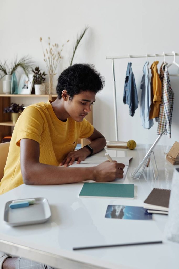 boy wearing yellow shirt while writing on white paper